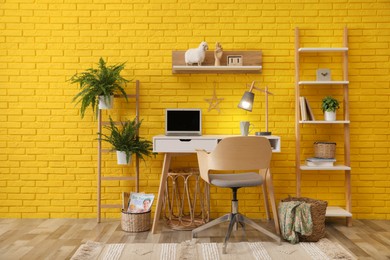 Photo of Modern workplace interior with wooden furniture and laptop near yellow brick wall