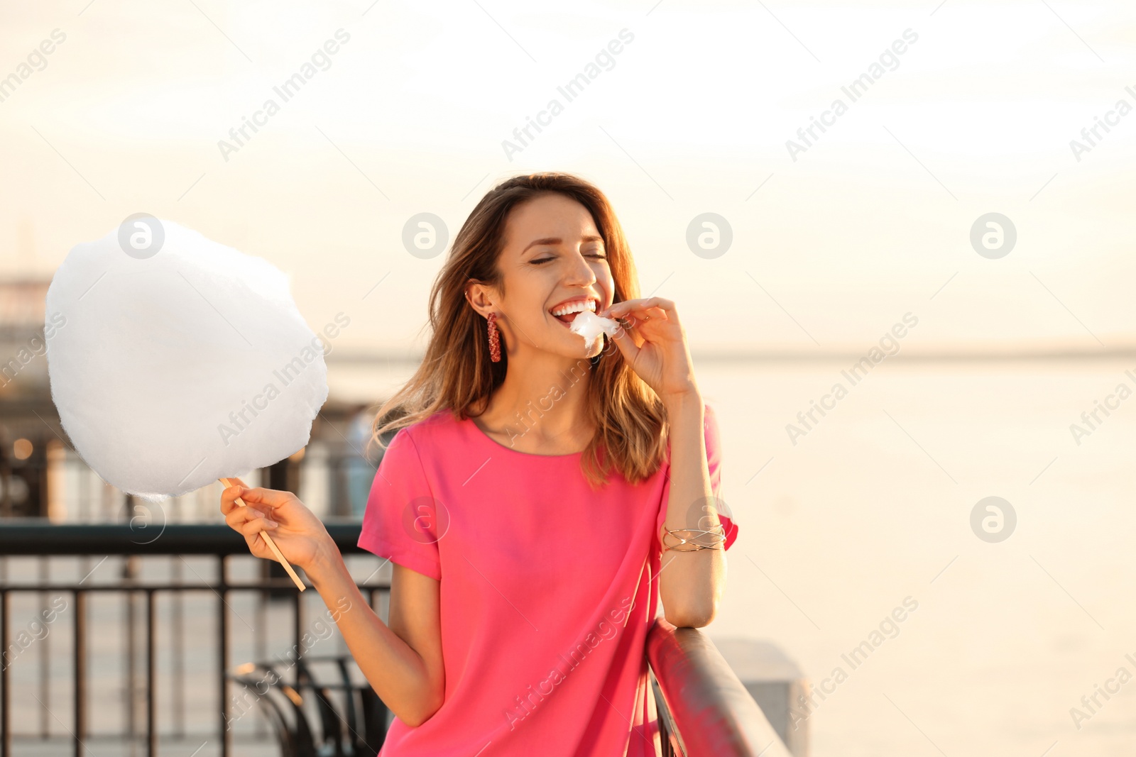 Photo of Happy young woman eating cotton candy on waterfront