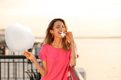 Happy young woman eating cotton candy on waterfront