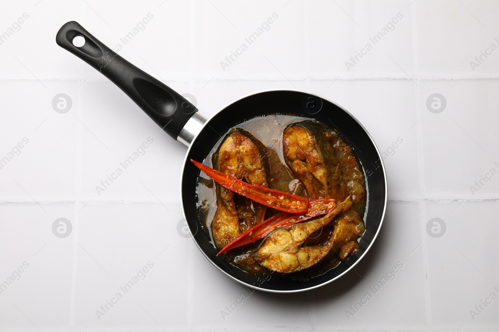 Photo of Tasty fish curry in frying pan on white tiled table, top view. Indian cuisine