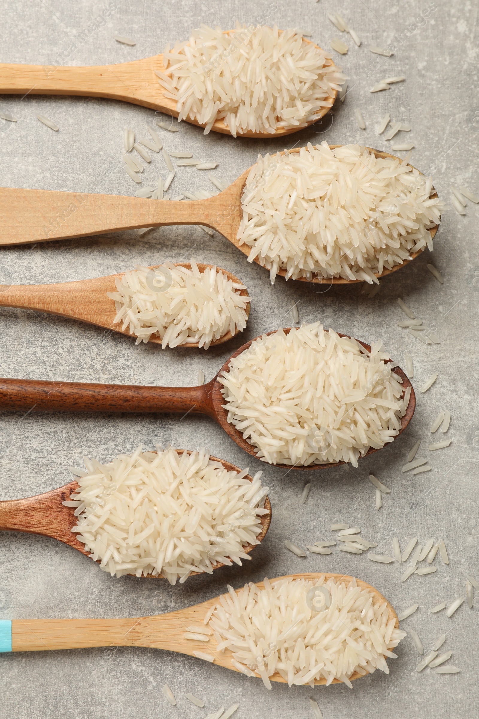 Photo of Raw basmati rice in spoons on grey table, flat lay