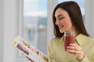 Photo of Beautiful young woman with delicious smoothie reading magazine at home