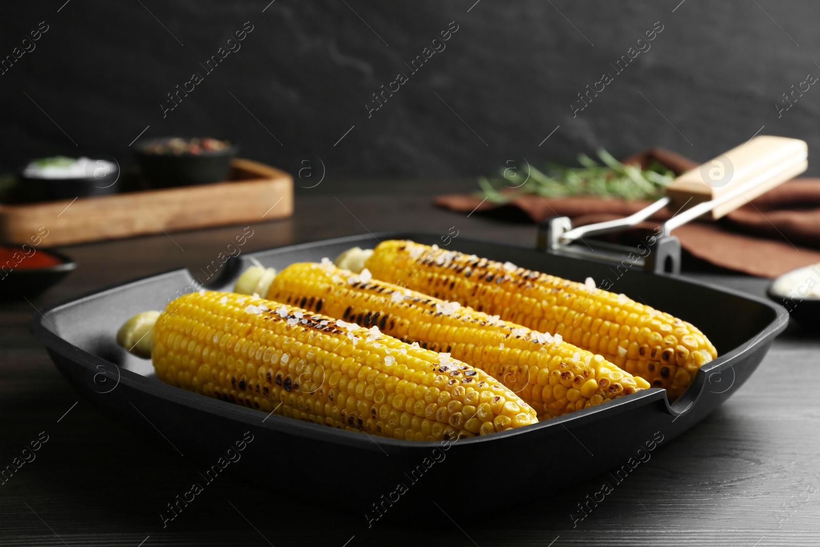Photo of Grill pan with tasty corn on dark grey wooden table, closeup