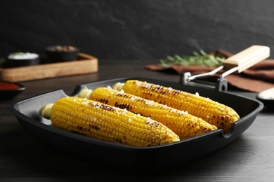 Photo of Grill pan with tasty corn on dark grey wooden table, closeup