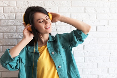 Portrait of beautiful woman listening to music with headphones near brick wall