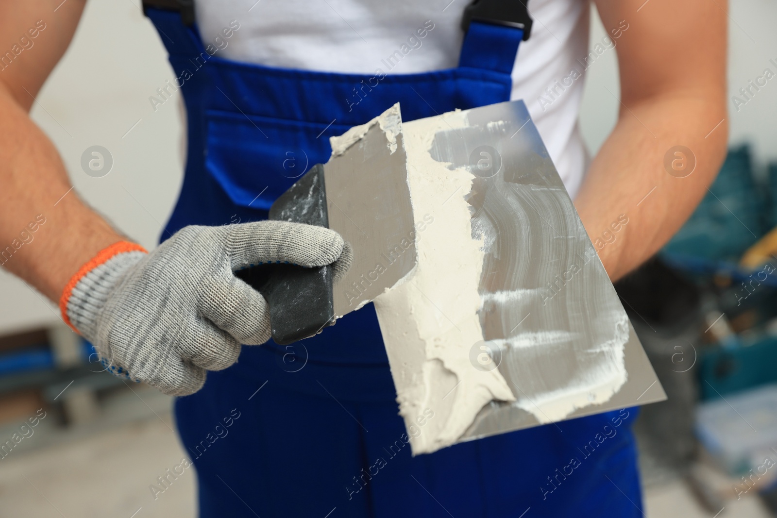 Photo of Worker with putty knives and plaster indoors, closeup
