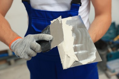 Worker with putty knives and plaster indoors, closeup