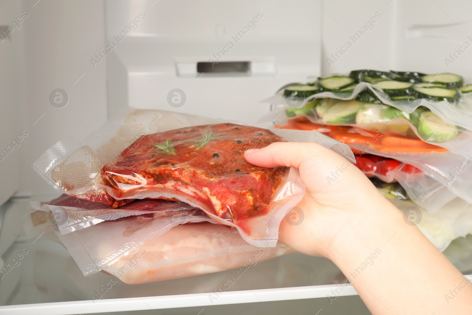 Photo of Woman putting vacuum packs with meat into fridge, closeup. Food storage