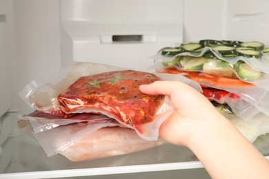 Photo of Woman putting vacuum packs with meat into fridge, closeup. Food storage