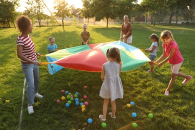 Photo of Group of children and teachers playing with rainbow playground parachute on green grass. Summer camp activity