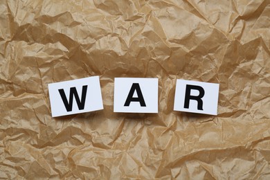Photo of Word War made of cards with letters on crumpled paper, top view