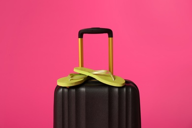 Stylish suitcase with flip flops on color background