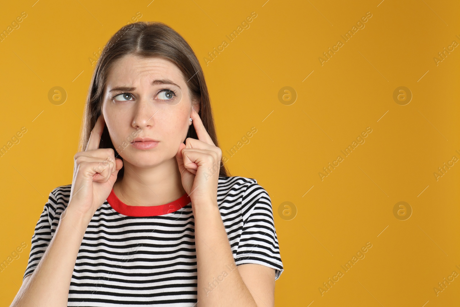 Photo of Emotional young woman covering her ears with fingers on yellow background. Space for text