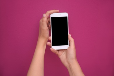 Photo of Young woman holding mobile phone with blank screen in hands on color background