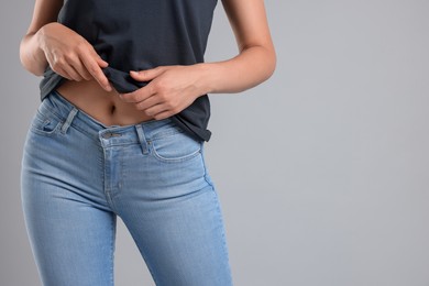 Woman wearing stylish jeans on light gray background, closeup. Space for text