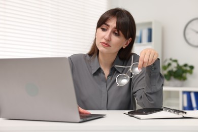 Overwhelmed woman sitting at table with laptop in office