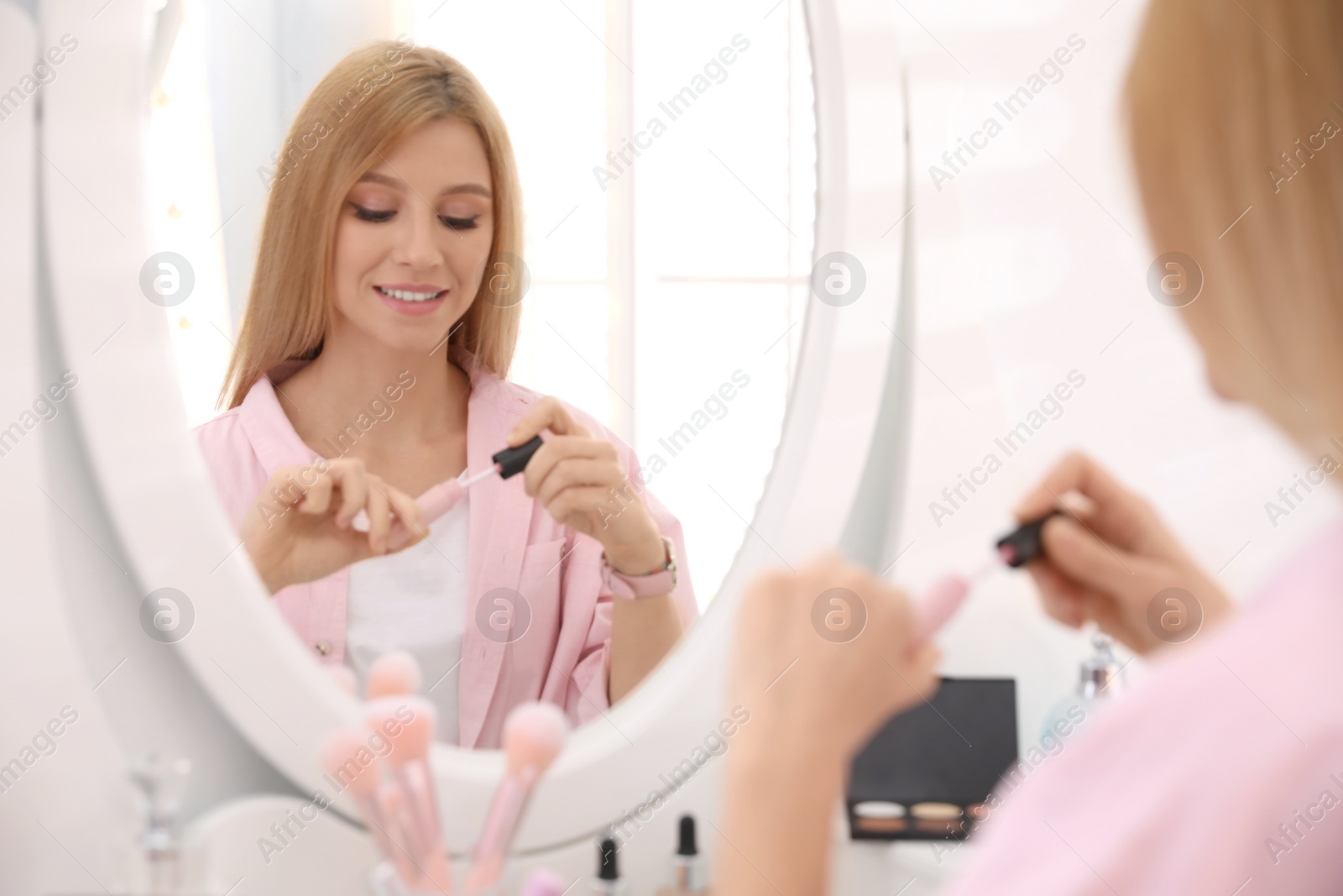 Photo of Beautiful young woman applying makeup near mirror indoors