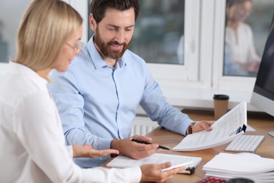 Photo of Happy businesspeople working with documents at table in office