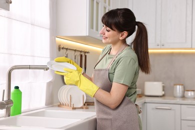Happy young housewife with clean plate in kitchen. Cleaning chores