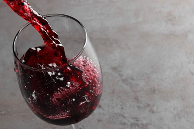 Photo of Pouring tasty red wine in glass at gray table, closeup. Space for text