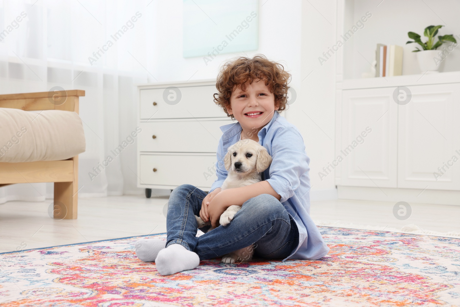 Photo of Little boy with cute puppy on carpet at home