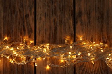 Glowing Christmas lights on wooden background, top view. Space for text