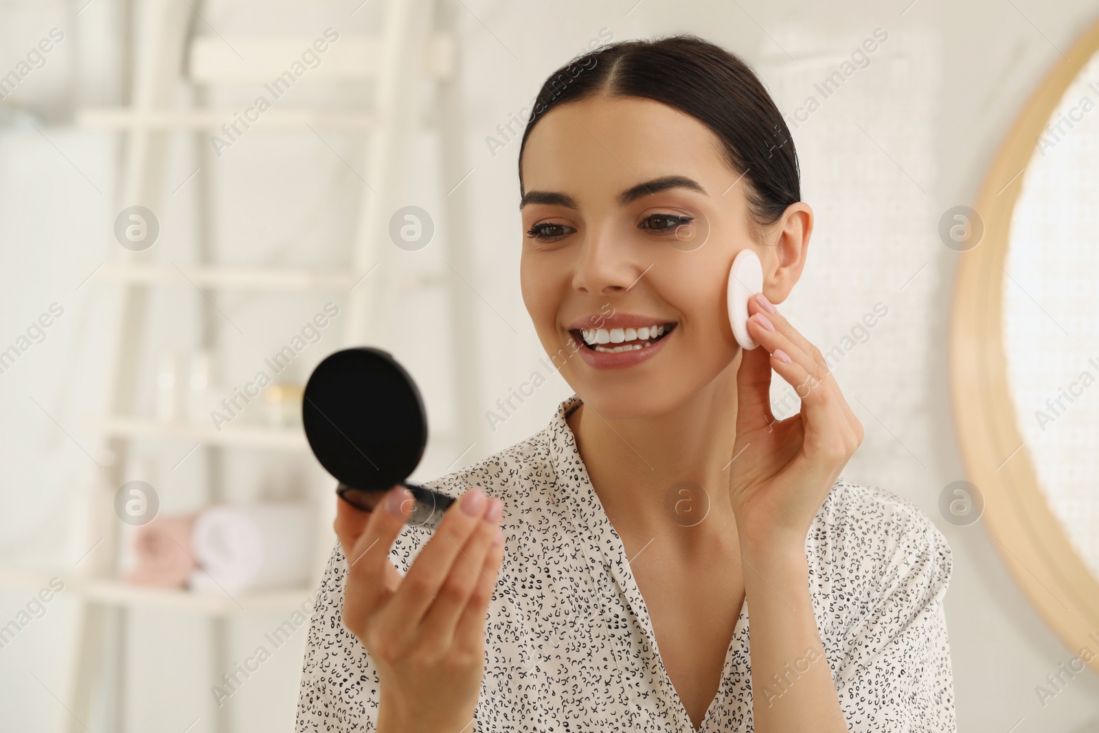 Photo of Beautiful young woman applying face powder with puff applicator in bathroom at home