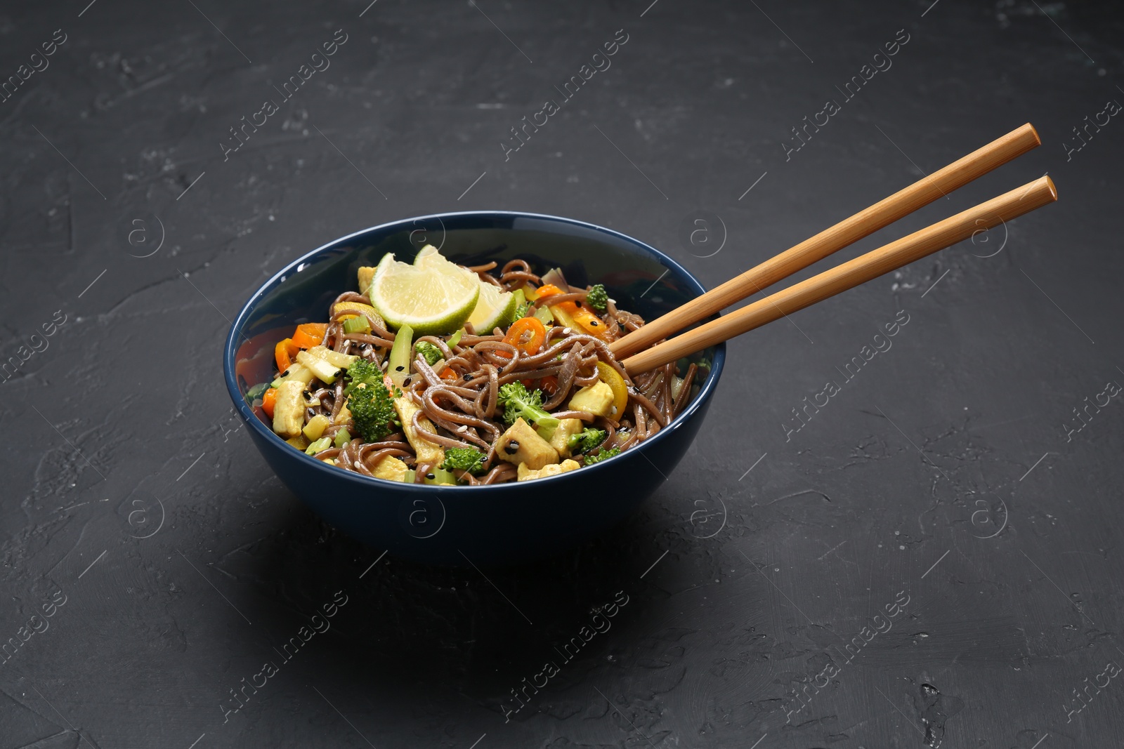 Photo of Stir-fry. Delicious cooked noodles with chicken and vegetables in bowl served on gray textured table