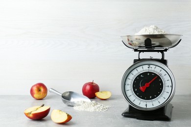 Photo of Kitchen scale with flour and ripe apples on grey table
