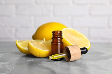 Photo of Bottle of essential oil with lemons on grey marble table against white brick wall, closeup