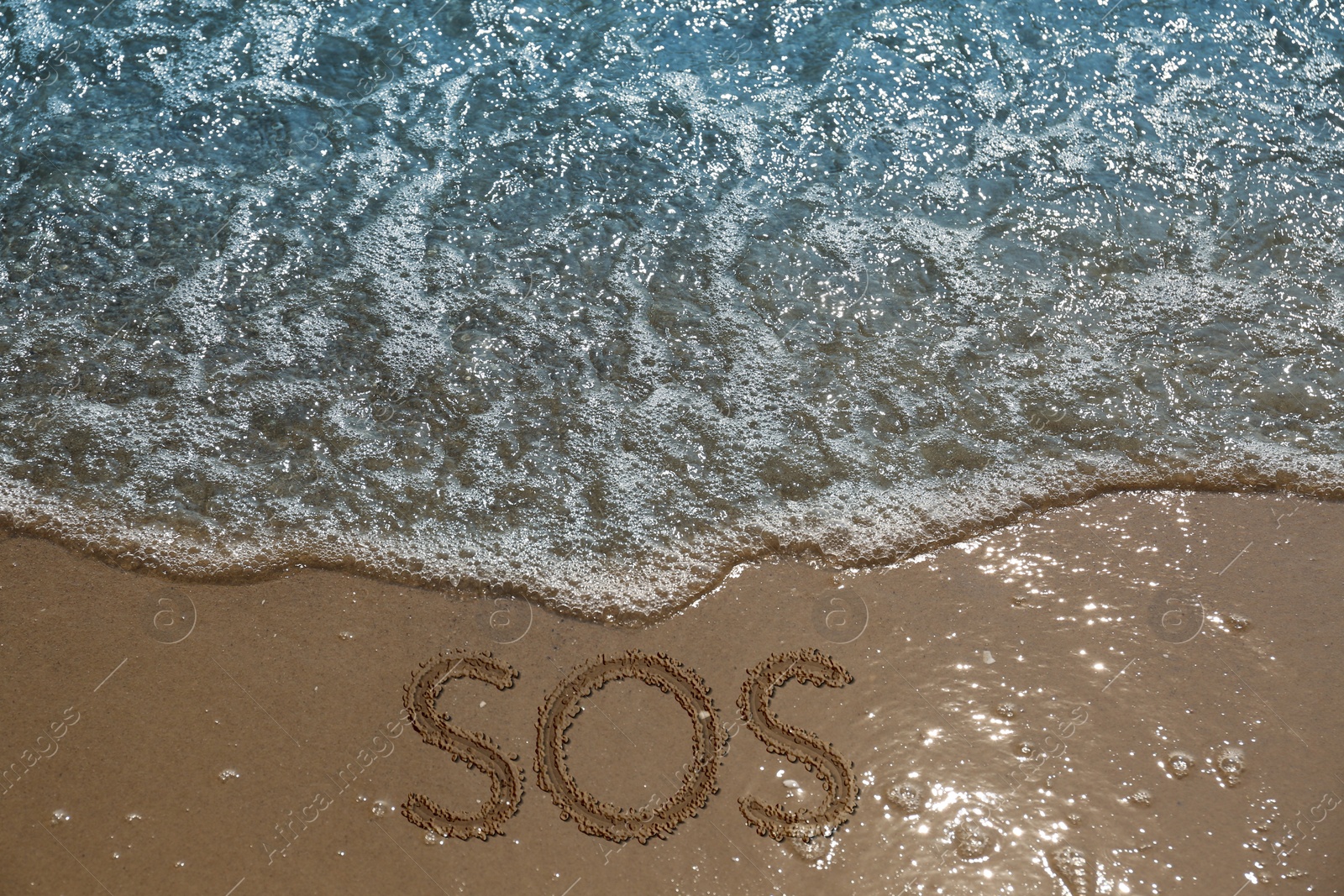 Image of SOS message drawn on sandy beach near sea, above view