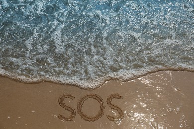 SOS message drawn on sandy beach near sea, above view