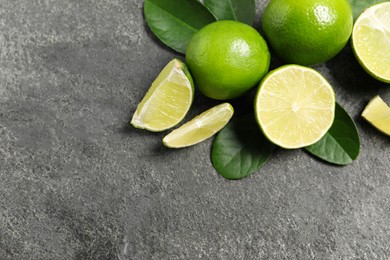 Fresh ripe limes and leaves on grey table, top view. Space for text