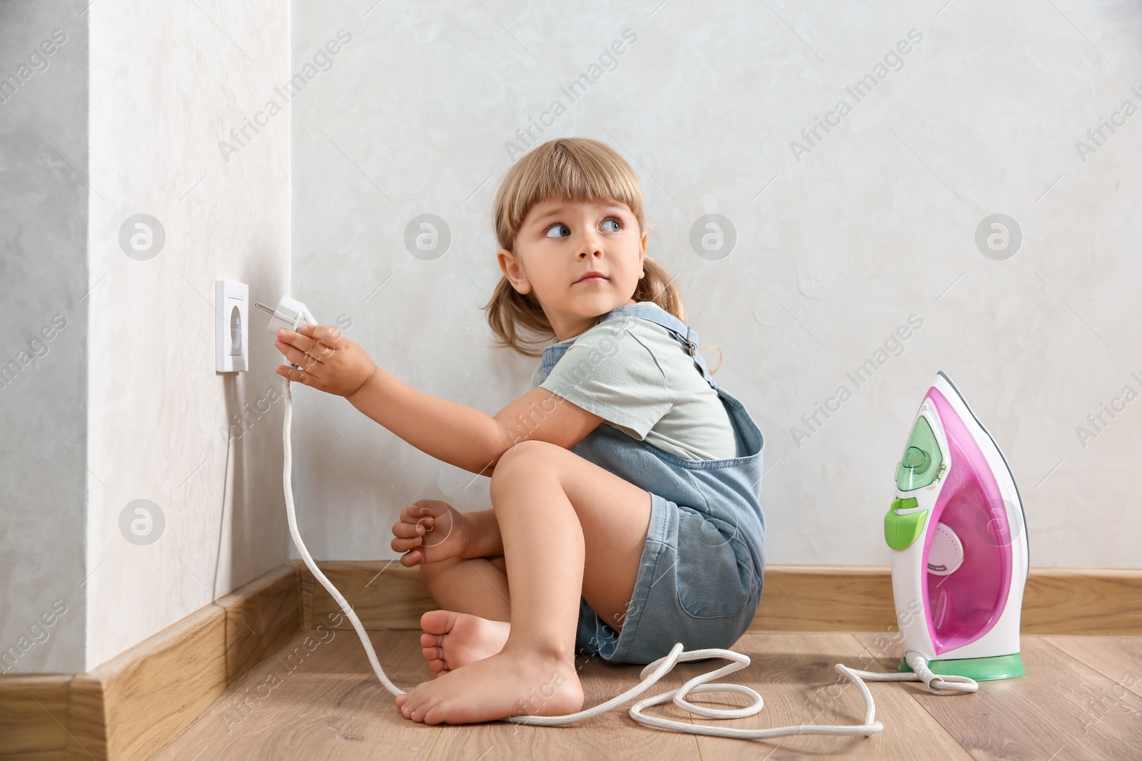 Photo of Little child playing with electrical socket and iron plug at home. Dangerous situation