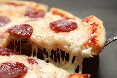 Taking slice of tasty pepperoni pizza on table, closeup