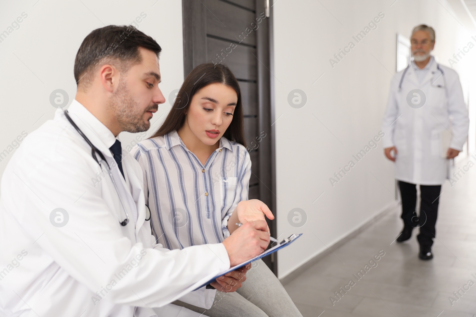 Photo of Doctor with clipboard consulting patient in clinic