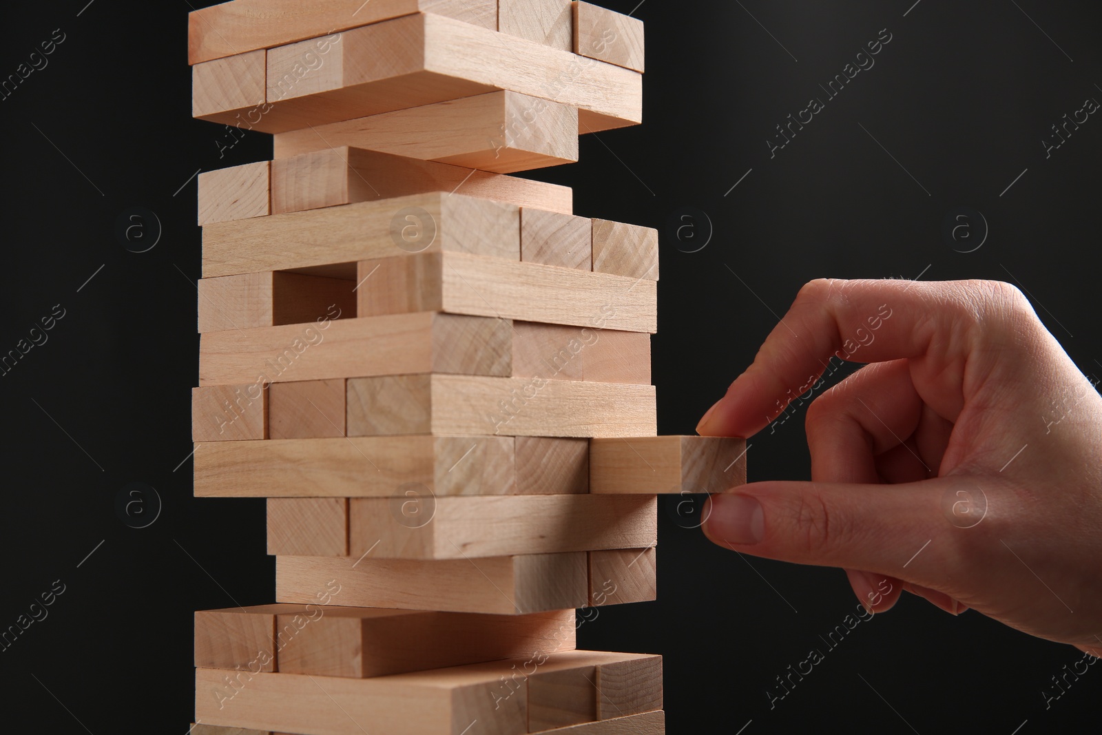 Photo of Woman playing Jenga on dark gray background, closeup