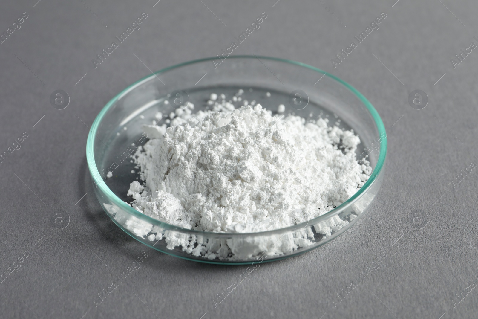 Photo of Petri dish with calcium carbonate powder on grey table