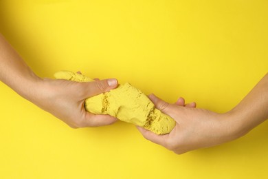Photo of Woman playing with kinetic sand on yellow background, top view
