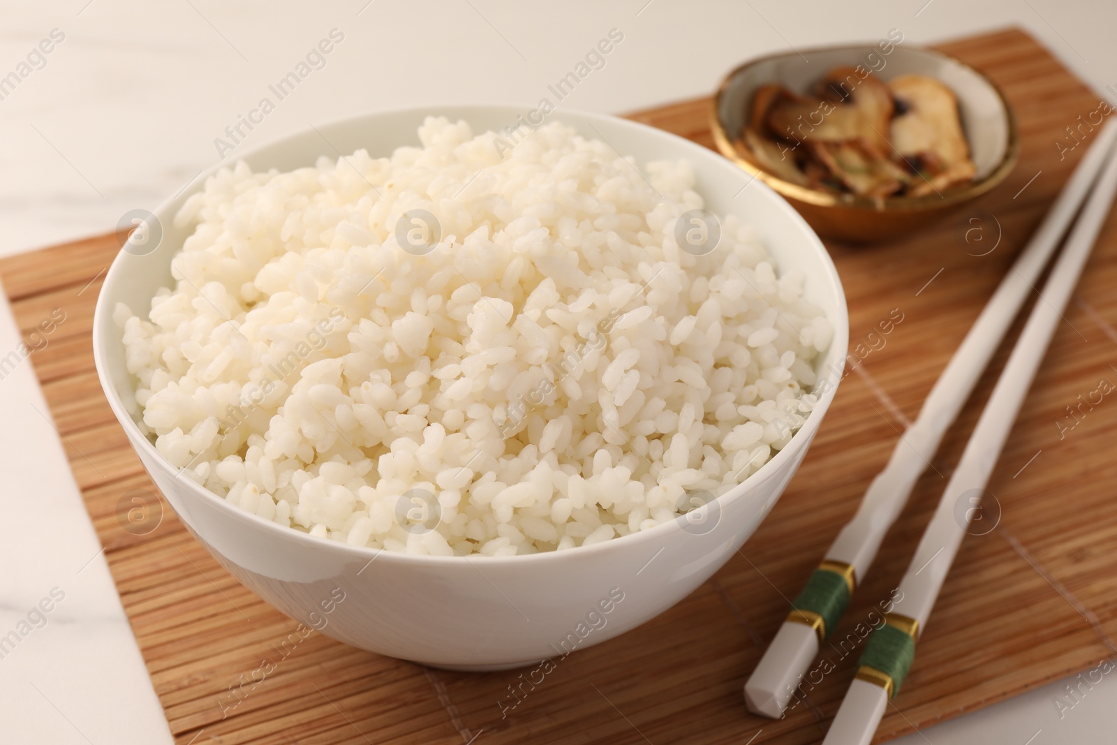 Photo of Bowl with delicious rice, mushrooms and chopsticks on white table, closeup