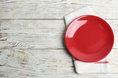 Photo of Empty red plate and napkin on white wooden table, flat lay. Space for text