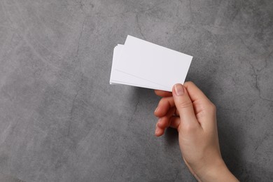 Photo of Woman holding blank cards at grey table, top view. Mockup for design