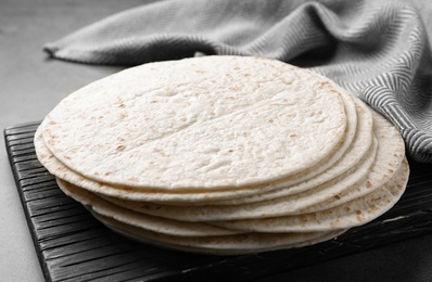 Photo of Wooden board with corn tortillas on table, closeup. Unleavened bread