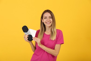 Photo of Happy young woman with disposable and reusable cloth menstrual pads on yellow background