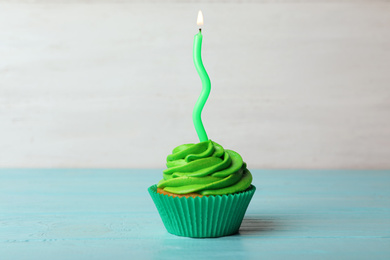 Delicious birthday cupcake with cream and burning candle on blue wooden table