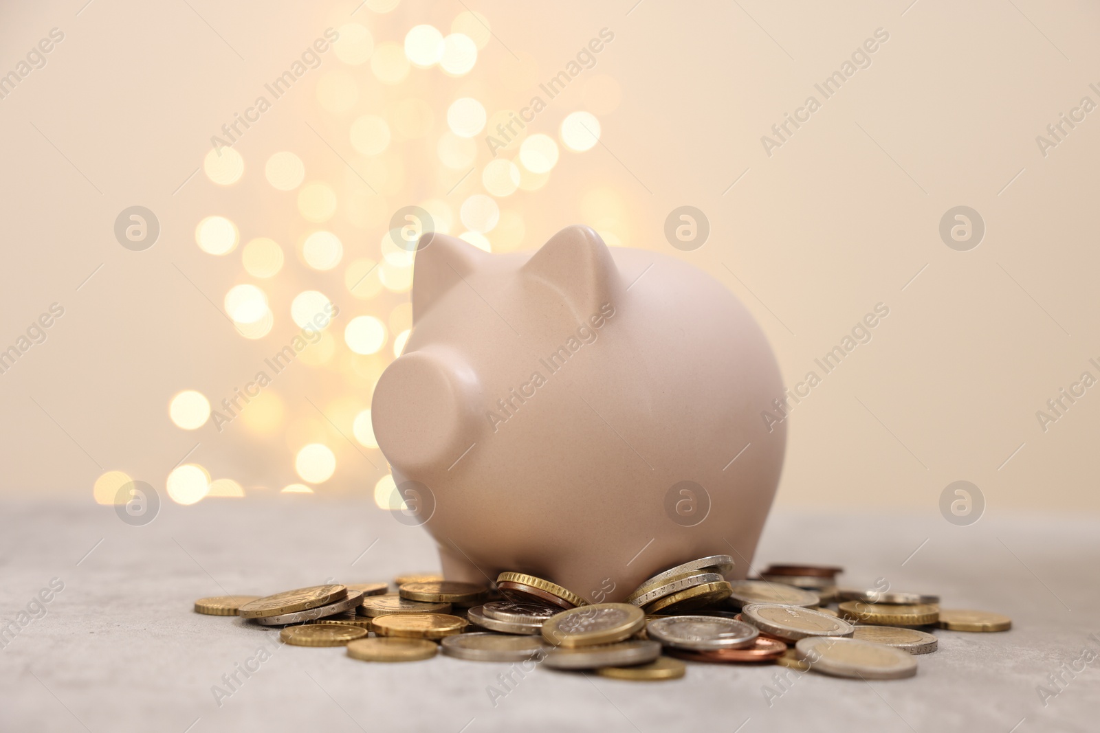 Photo of Piggy bank and coins on grey table against blurred lights