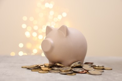 Photo of Piggy bank and coins on grey table against blurred lights