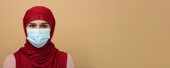 Image of Portrait of Muslim woman in hijab and medical mask on beige background, space for text. Banner design
