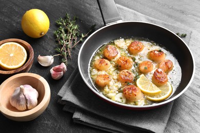 Photo of Delicious scallops with sauce in frying pan and ingredients on dark gray textured table, closeup