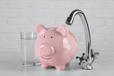 Water scarcity concept. Piggy bank, tap and glass of drink on white table